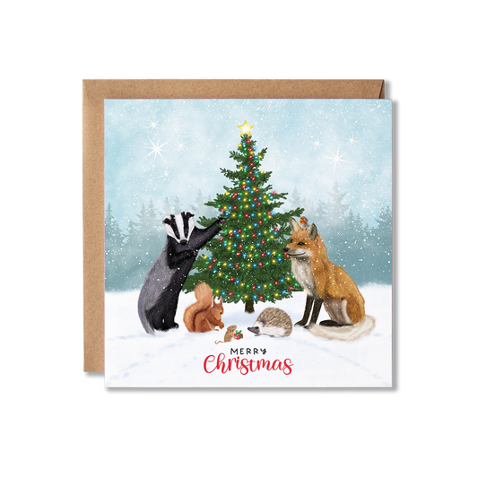 Christmas card with illustration of a group of British woodland animals, badger, fox, hedgehog, red squirrel, mouse and a robin gathered around a Christmas tree with lights on and the mouse holding a tiny present, with the message Merry Christmas.