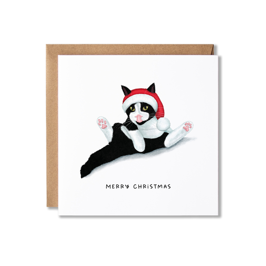 Christmas card with illustration of a black and white cat sat in a funny position having a wash wearing a red and white Santa hat with the message Merry Christmas.