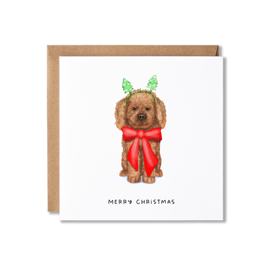 Christmas card with illustration of a Cavapoo dog sat in a big red ribbon bow and wearing Christmas tree bobblers with the message Merry Christmas.