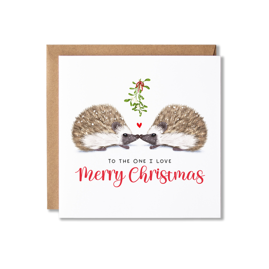 Christmas card with illistration of a couple of hedgehogs sitting underneath some springs of mistletoe tied in a red ribbon with a small red heart shape between them, with the message To The One I Love Merry Christmas.