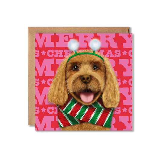 A tan cockerpoo dog in a fluffy snowball headband and red and green knitted scarf with a Merry Christmas background