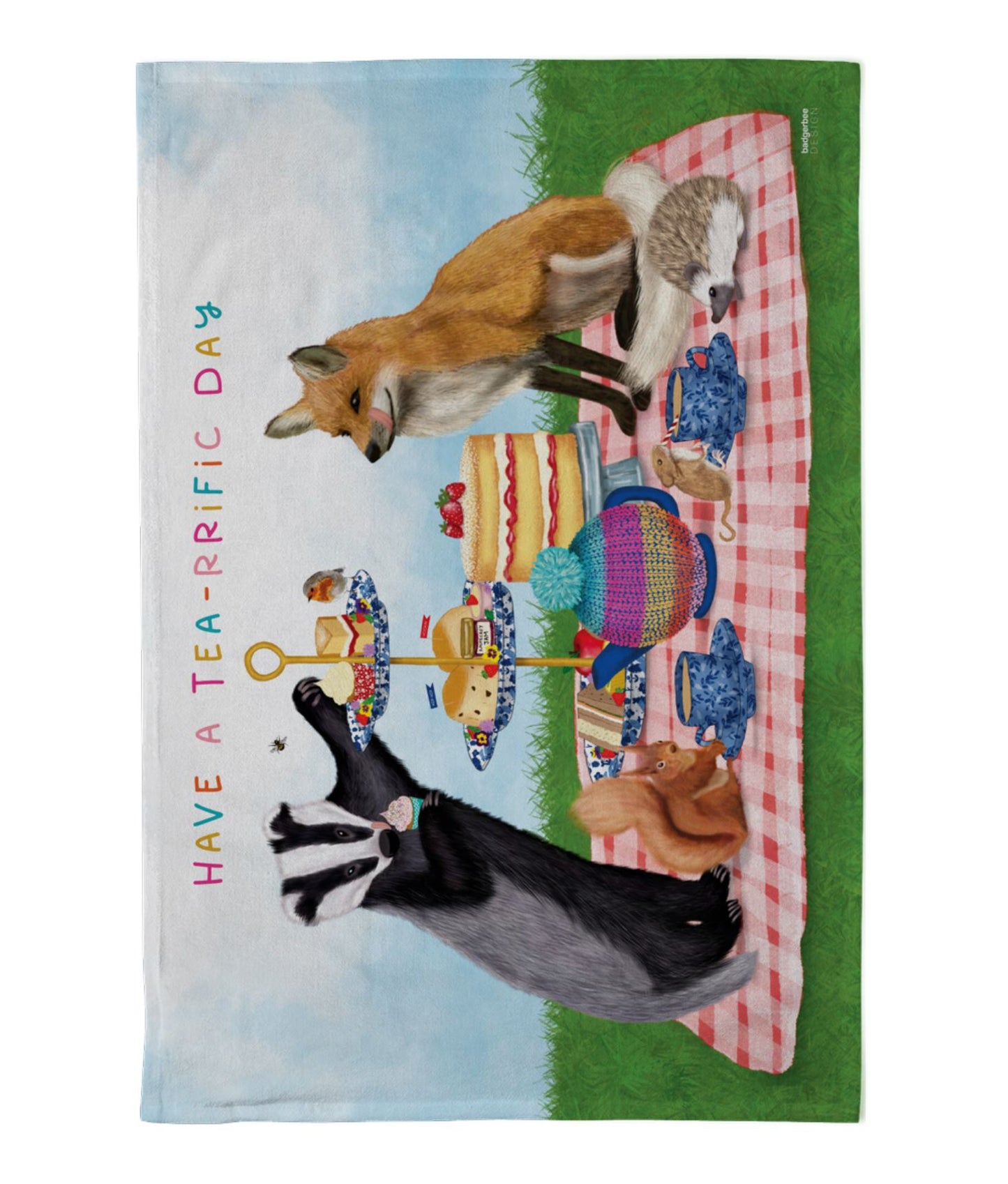 Tea towel with fox and badger having afternoon tea with a hedgehog. red squirrel, mouse and a robin and text 'Have a tea-riffic day' on a checked tablecloth background.