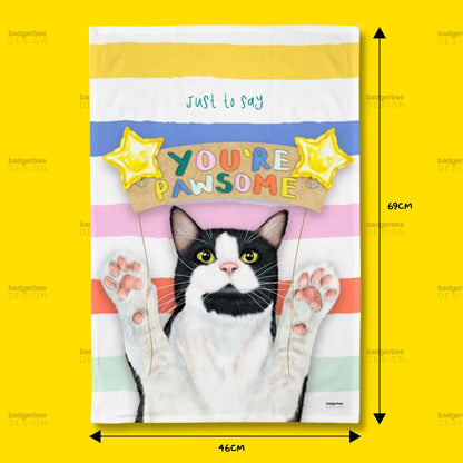A rectangular printed Tea Towel against a bright yellow background, with dimension arrows and labels indicating 69 cm height and 46 cm width. The product has horizontal pastel stripes in yellow, white, blue, pink, and mint, a black-and-white cat illustration with raised paws, and the text 'just to say YOU'RE PWSOME' with yellow star graphics.