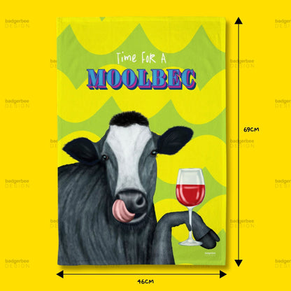 A rectangular printed tea towel featuring an illustration of a cow holding a glass of red wine, with the text 'Time FOR A MOOLBEC' on a bright yellow background. Black dimension arrows and labels indicate 69 cm height and 46 cm width.