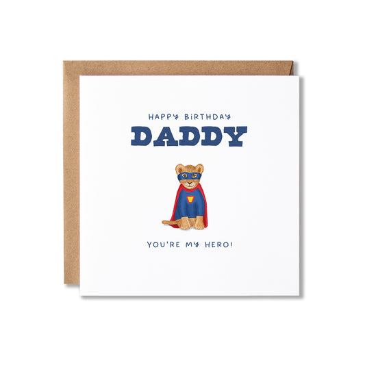 A square birthday card with a kraft envelope, featuring a lion cub dressed as a superhero with the text 'HAPPY BIRTHDAY DADDY' and 'YOU'RE MY HERO!'.