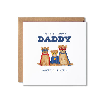 A square birthday card with a kraft envelope, featuring an illustration of three lion cubs superheroes in red and blue costumes under the text 'HAPPY BIRTHDAY DADDY' and 'YOU'RE OUR HERO!'.