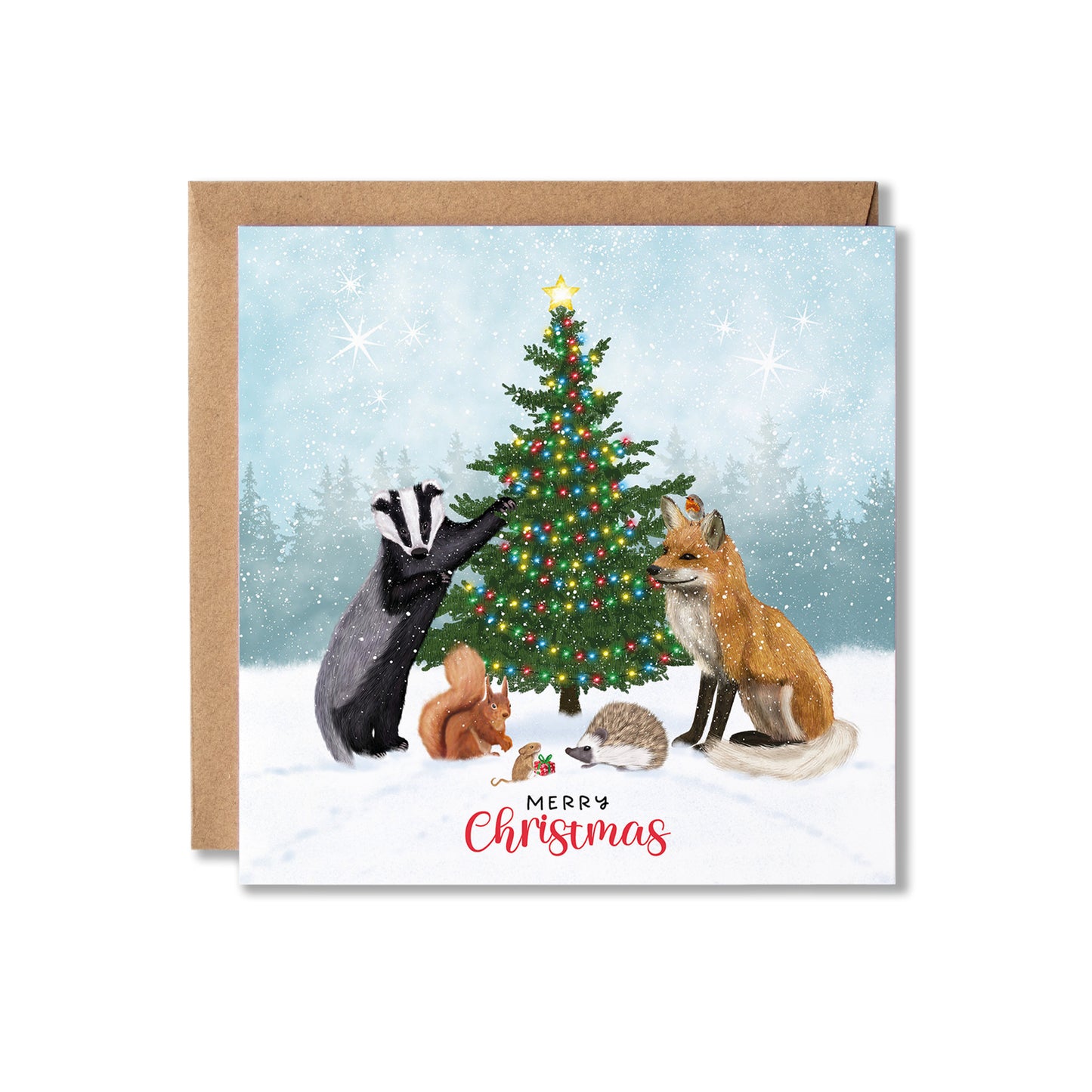 A square Christmas greeting card with a kraft envelope, featuring an illustrated winter scene with a decorated tree, a badger, a fox, and small woodland animals in the snow. The card reads 'Merry Christmas' at the bottom.
