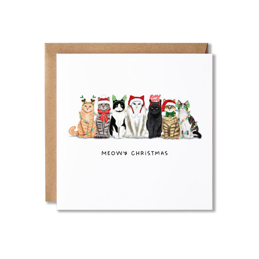 A square greeting card with a brown kraft envelope behind it, featuring an illustration of seven cats wearing Christmas hats and scarves, with the text 'MEOWY CHRISTMAS' below. The card is photographed on a clean white background.