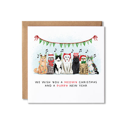 A square white greeting card with a brown kraft envelope behind it, featuring an illustration of six cats and a dog wearing Christmas hats under a green bunting garland. The text at the bottom reads, 'WE WISH YOU A MEOW'S CHRISTMAS AND A PURRY NEW YEAR'.