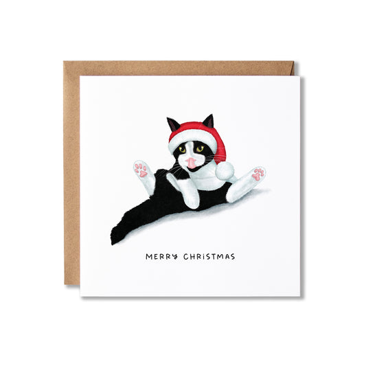 A square Christmas greeting card with a brown envelope behind it, featuring an illustration of a black-and-white cat wearing a red Santa hat on a white card, with the text 'MERRY CHRISTMAS' below.