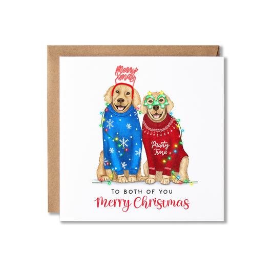 A square Christmas greeting card with a kraft envelope behind it. The card features an illustration of two golden retrievers wearing colourful holiday sweaters and masks, with the text 'Merry Christmas' and 'TO BOTH OF YOU Merry Christmas' printed below.
