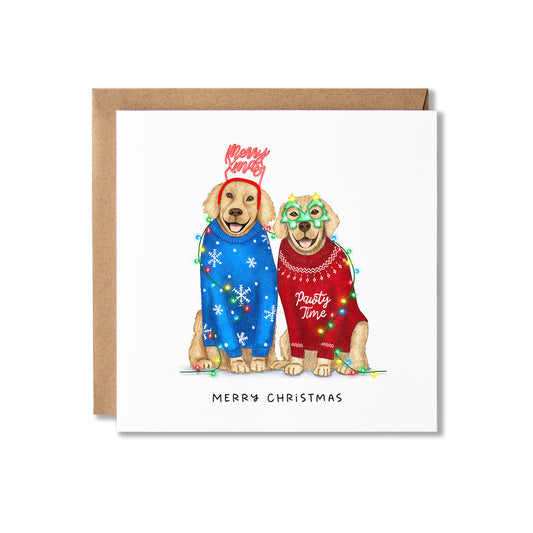 A square Christmas greeting card with a kraft envelope behind it. The card features an illustration of two golden retriever dogs wearing colorful holiday sweaters and string lights, with 'Merry Christmas' printed at the bottom.
