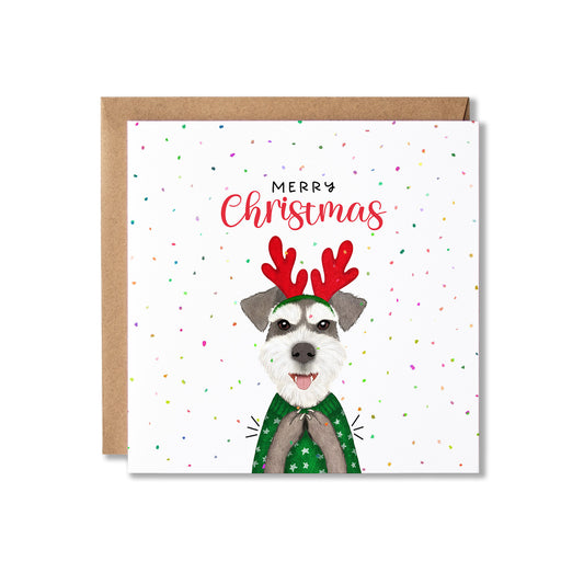 A square Christmas greeting card with a kraft envelope behind it. The card features a white background with colorful confetti dots, the text 'MERRY Christmas' in black and red script, and an illustration of a dog wearing a green sweater and red reindeer antlers.
