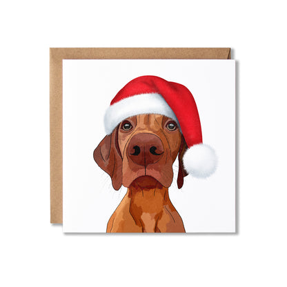 A square greeting card featuring an illustration of a Hungarian Vizsla dog wearing a red Santa hat, shown with a brown kraft envelope on a white background.