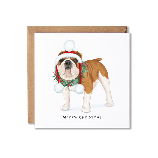 A square Christmas greeting card featuring an illustrated brown and white bulldog wearing a Santa hat and green wreath, with the text 'MERRY CHRISTMAS' below. The card is shown with a brown kraft envelope behind it on a white background.