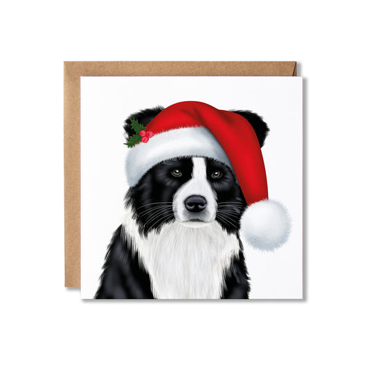 A square greeting card featuring a black and white dog wearing a red Santa hat with a white pom-pom and small holly sprig, shown with a brown kraft envelope behind it on a white background.