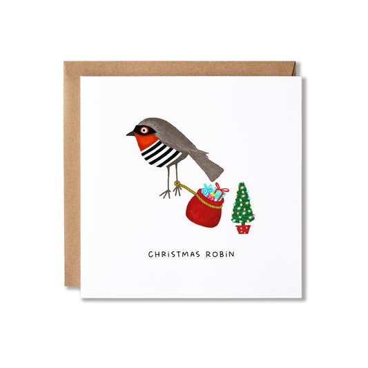 A square white greeting card with a kraft brown envelope behind it, featuring an illustration of a Christmas robin dressed as a 'robber' holding a red gift sack next to a small decorated tree, with the text 'CHRISTMAS ROBIN' below.