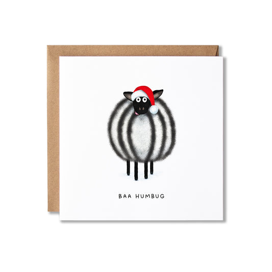 A square white greeting card with a brown kraft envelope behind it, featuring a cartoon sheep with black and white stripes wearing a red Santa hat and the text 'BAA HUMBUG' below.