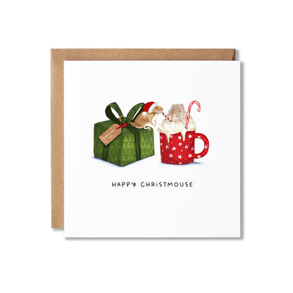 A square Christmas greeting card with a kraft envelope, featuring an illustration of a green gift box  with a gift tag that says 'with love xx' and a small Christmas mouse sitting on top and drinking from a red and white straw, hot chocolate from red mug with whipped cream and candy canes, with the text 'HAPPY CHRISTMOUSE' below.