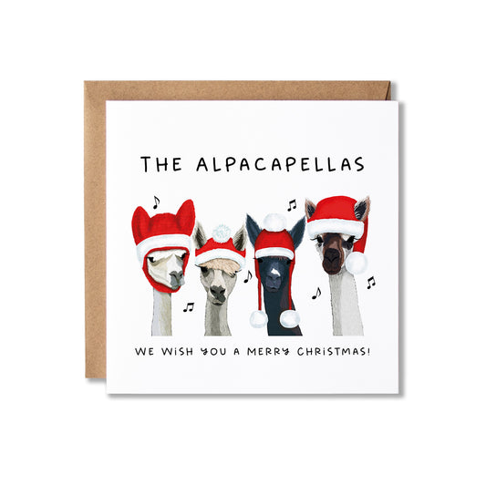 A square Christmas greeting card with a kraft envelope behind it. The card features an illustration of four alpaca heads wearing Santa hats, with the text 'THE ALPACAPELLAS' at the top and 'WE WISH YOU A MERRY CHRISTMAS!' at the bottom.