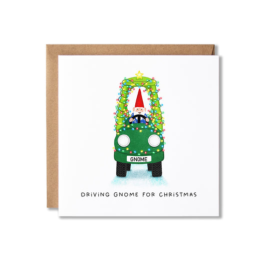 A square white greeting card with a brown kraft envelope behind it, featuring an illustration of a gnome driving a green car wrapped in Christmas lights, with the text 'DRIVING GNOME FOR CHRISTMAS' below.