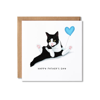 A square Father's Day greeting card with a brown envelope behind it. The card features an illustration of a black-and-white cat lying down and holding a light blue heart-shaped balloon, with the text 'HAPPY FATHER'S DAY' printed below.