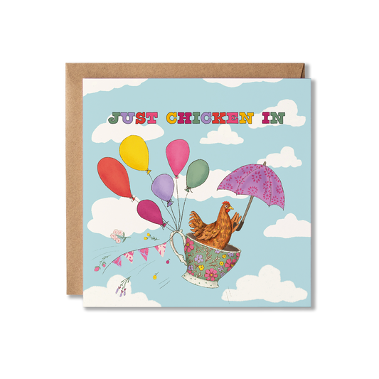 Illustration of a chicken sitting in a floral teacup flying through a cloudy sky being held up with balloons and an umbrella, with the words Just Chicken In above in colourful letters. Thinking of You greeting card.