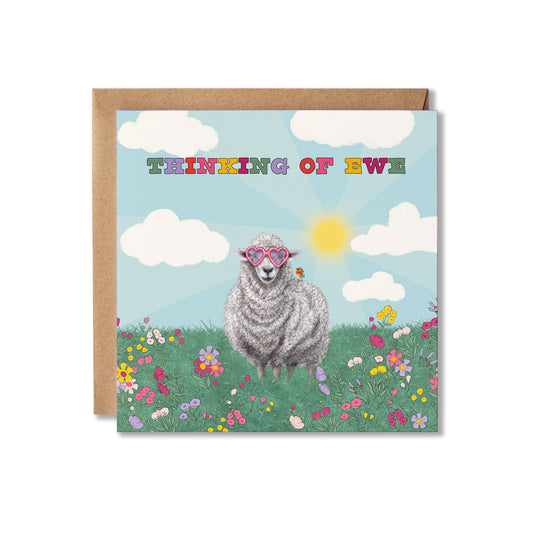 Square greeting card with an illustration of a sheep wearing heart shape glasses in a field of flowers and clouds, with 'Thinking of Ewe' text.