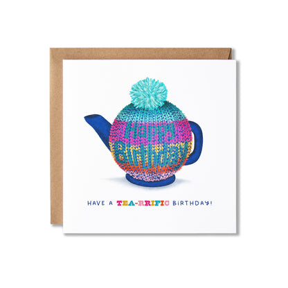 A square birthday card with a kraft envelope, featuring a colourful knitted teapot cosy on a teapot illustration and the text 'HAVE A TEA-RIFIC BIRTHDAY!' on a white card background.
