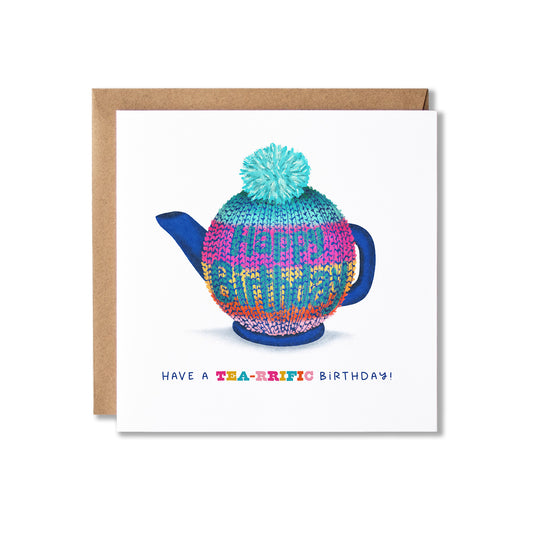 A square birthday card with a kraft envelope, featuring a colourful knitted teapot cosy on a teapot illustration and the text 'HAVE A TEA-RIFIC BIRTHDAY!' on a white card background.