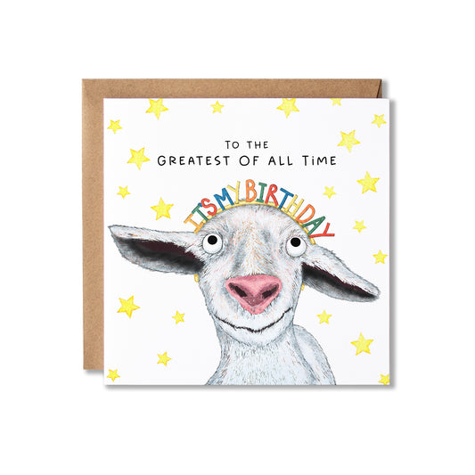A square greeting card with a brown envelope behind it, featuring a white goat illustration, yellow stars, and the text 'TO THE GREATEST OF ALL TIME IT'S BIRTHDAY' on a white background.