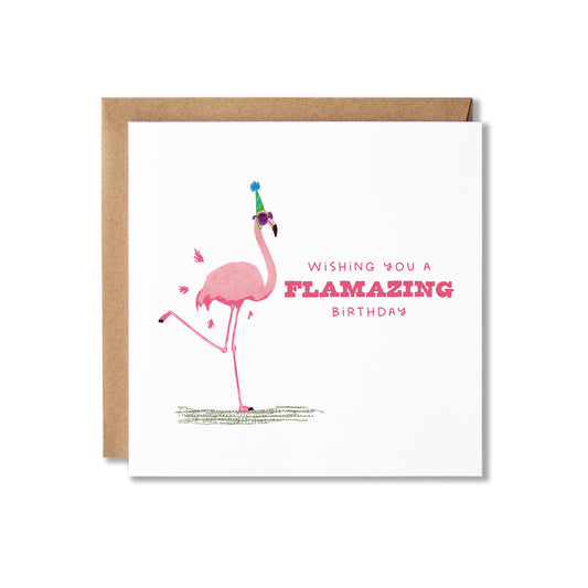 A square white greeting card with a brown kraft envelope behind it, featuring a pink flamingo wearing a party hat and the text 'WISHING YOU A FLAMAZING BIRTHDAY' in pink lettering.