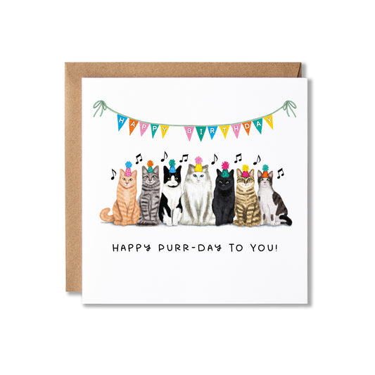 A square greeting card with a kraft envelope behind it, featuring seven illustrated cats wearing party hats under a colourful bunting banner that reads 'Happy Birthday.' The card text at the bottom says 'Happy Purr-Day to You!' on a white background.
