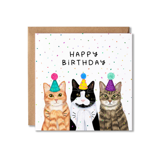A square birthday card with a kraft envelope behind it, featuring three illustrated cats wearing party hats under the words 'HAPPY BIRTHDAY' on a white background with scattered confetti.
