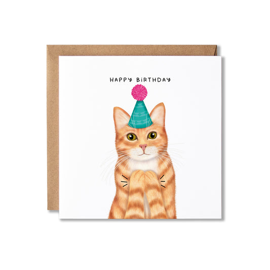 A square birthday card with a white front featuring an illustrated orange tabby cat wearing a teal party hat with a pink pom-pom, clapping, with the text 'HAPPY BIRTHDAY' above. A brown kraft envelope is placed behind the card on a white background.