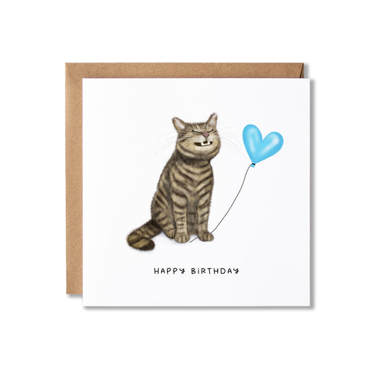 A square birthday card with a brown kraft envelope, featuring an illustration of a grinning tabby cat sitting next to a light blue heart-shaped balloon and the text 'HAPPY BIRTHDAY' below.