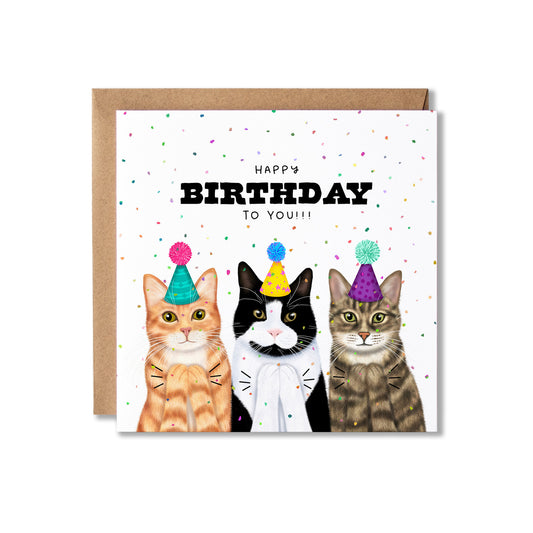 A square greeting card with a brown envelope behind it, featuring three illustrated cats wearing party hats and the text 'HAPPY BIRTHDAY TO YOU!!' on a white background with scattered confetti.