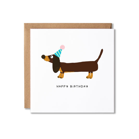 A square birthday card with a kraft envelope, featuring an illustration of a dachshund wearing a party hat above the words 'HAPPY BIRTHDAY'.