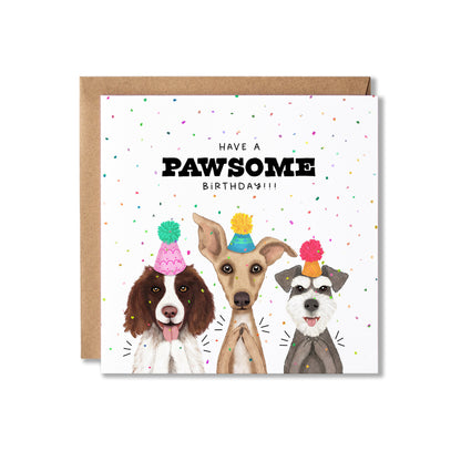 A square birthday card with a kraft envelope behind it, featuring three illustrated dogs wearing party hats against a white background with scattered confetti. The card reads 'HAVE A PAWSOME BIRTHDAY!!!' in black text.