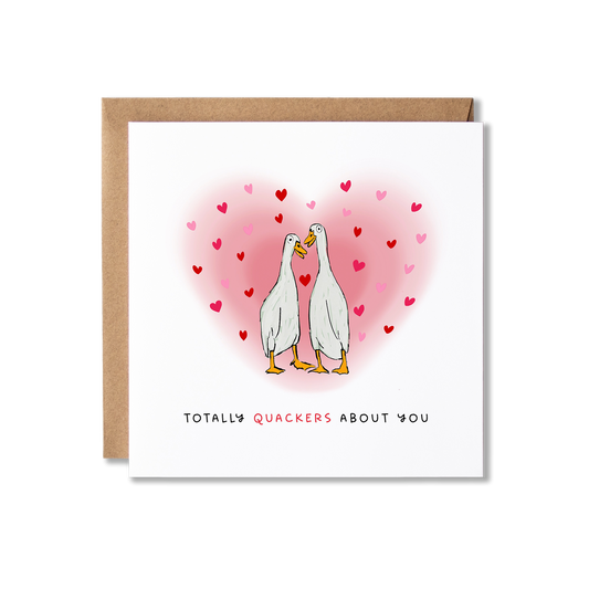 Greeting card with illustration of two white ducks looking at each other surrounded by a hug pink heart with the message Totally Quackers About You.