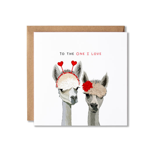 A square greeting card with a kraft paper envelope, featuring an illustration of two alpacas wearing red heart and flower headbands, with the text 'TO THE ONE I LOVE' above them.