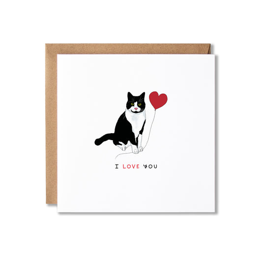 A square white greeting card with a brown kraft envelope behind it, featuring a black-and-white cat holding a red heart and the words 'I LOVE YOU' printed below.
