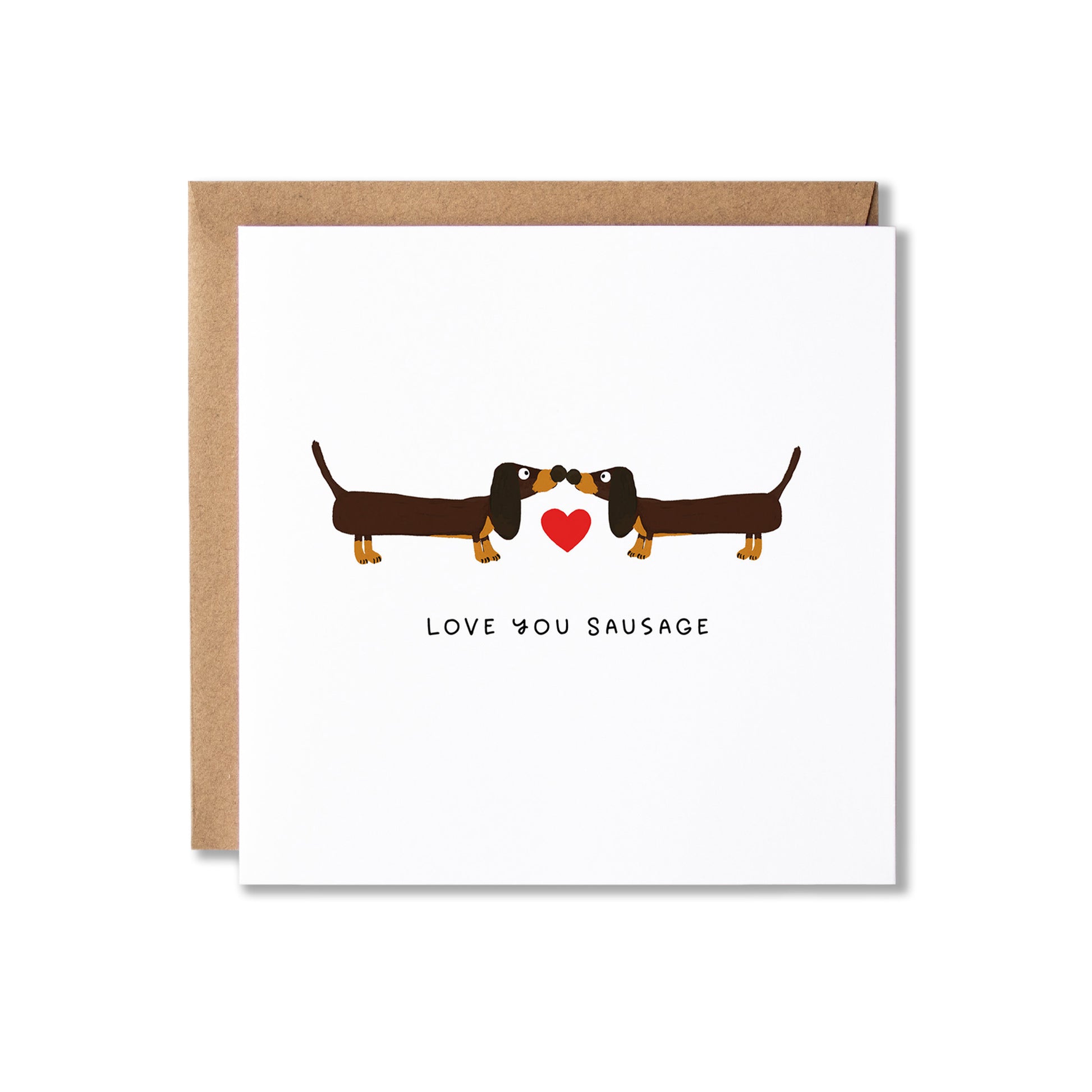 A white greeting card with a brown kraft envelope behind it, featuring a cartoon dachshund facing another dachshund with a small red heart between them and the text 'LOVE YOU SAUSAGE' below.