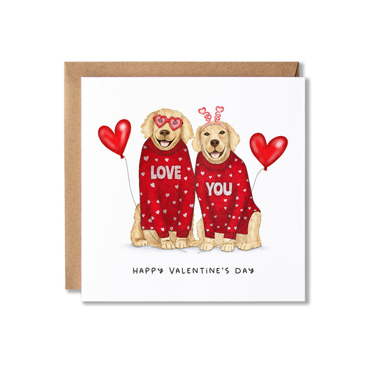 A square Valentine's Day greeting card with a kraft envelope behind it. The card features an illustration of two golden retriever dogs wearing red hearts-patterned sweaters, one reading 'LOVE' and the other 'YOU', each holding a red heart balloon.