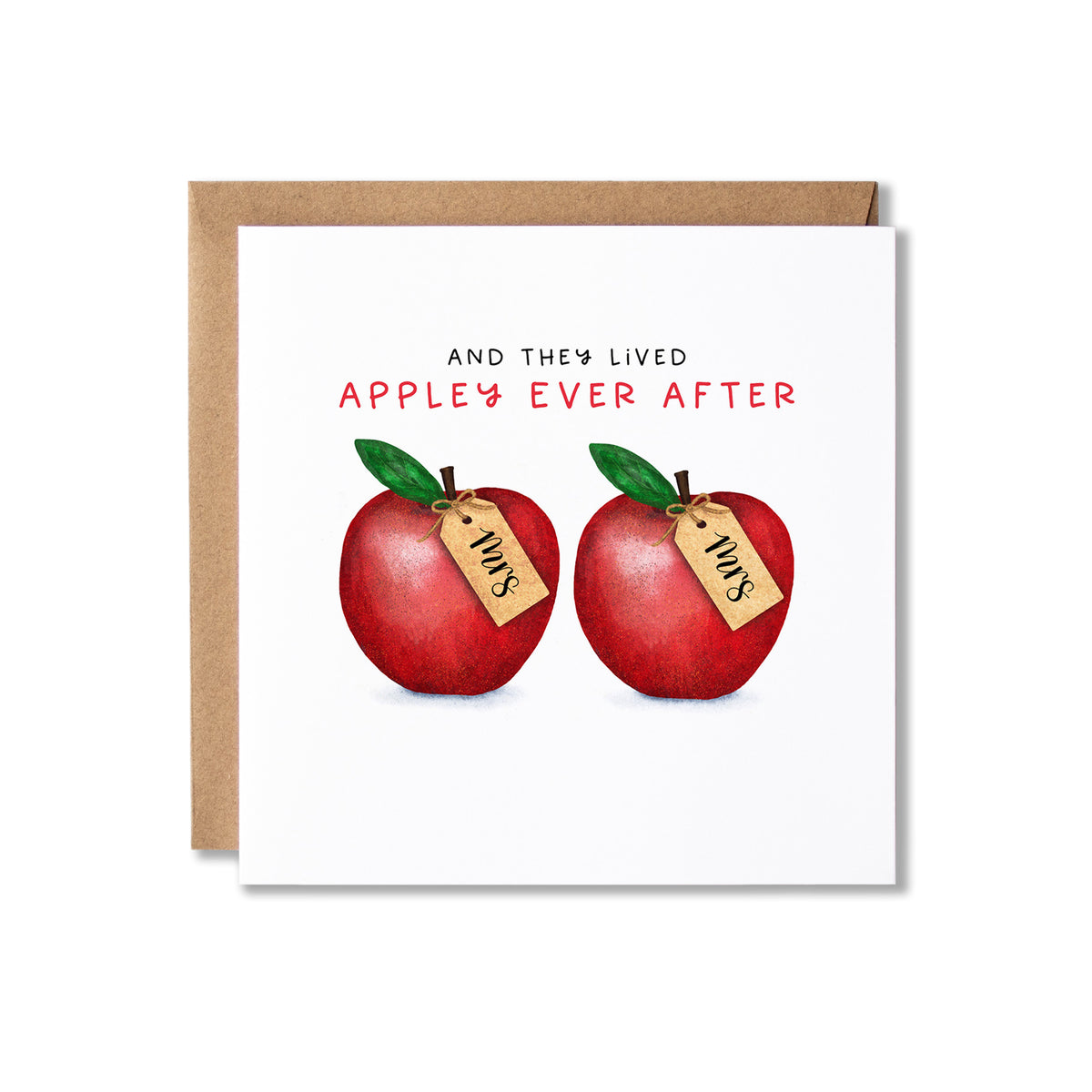 A square greeting card with a kraft envelope behind it, featuring the text 'AND THEY LIVED APPLE'S EVER AFTER' above two red apples with green leaves and small tags reading 'Mrs'.