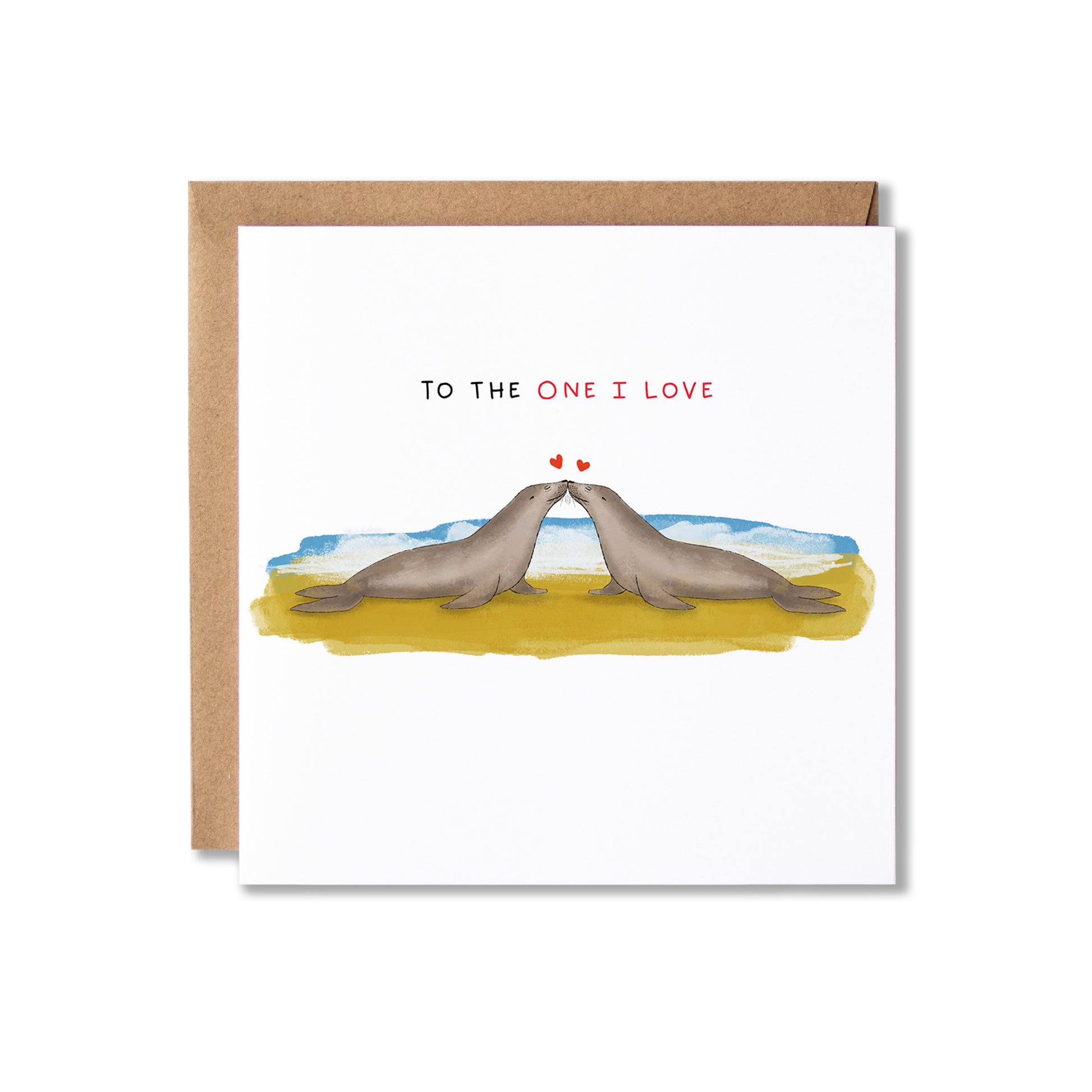 A square greeting card with a brown kraft envelope, featuring an illustration of two seals facing each other on a yellow beach with blue water and the text 'TO THE ONE I LOVE' above them.