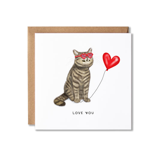 A square greeting card with a brown kraft envelope behind it, featuring an illustration of a grey tabby cat wearing red heart-shaped sunglasses and holding a red heart balloon, with the words 'LOVE YOU' printed below.
