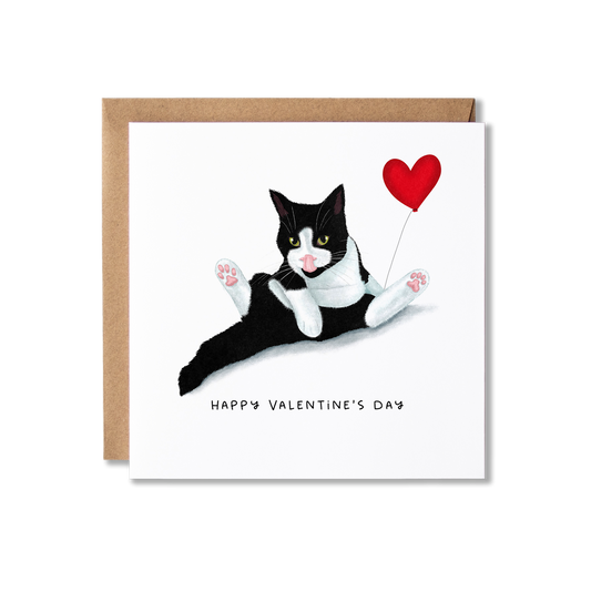 Black and white tuxedo cat sat licking, holding a red heart shaped balloon with the words Happy Valentine's Day written underneath.
