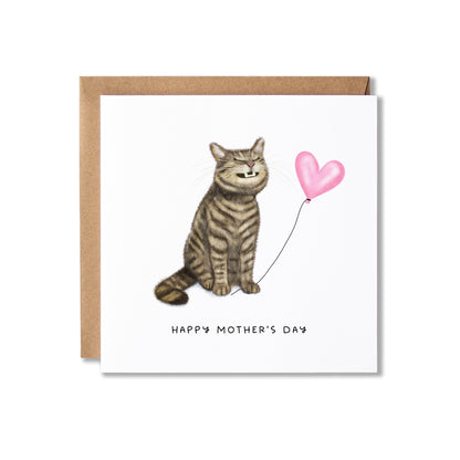 A square Mother's Day greeting card with a brown kraft envelope behind it. The card features an illustration of a brown tabby cat sitting and holding a pink heart-shaped balloon, with the text 'HAPPY MOTHER'S DAY' printed below.