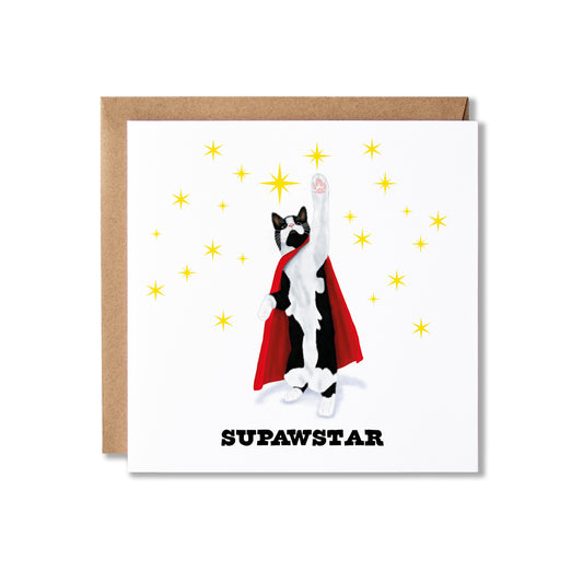 A square greeting card with a brown kraft envelope behind it, featuring a white front design with a black-and-white cat in a red cape surrounded by yellow stars and the word 'SUPAWSTAR' in black text.